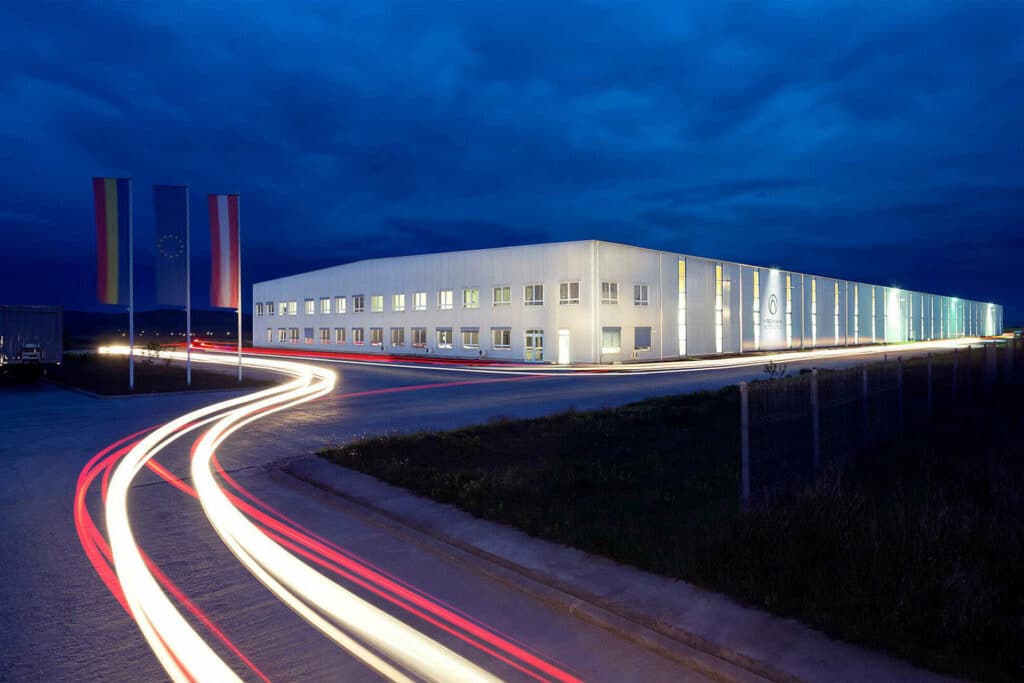Nachtaufnahme des Firmengebäudes von Hirschmann Automotive – Standort mit industrieller Automatisierungs-Förderungstechniklösung tv on Robotunits