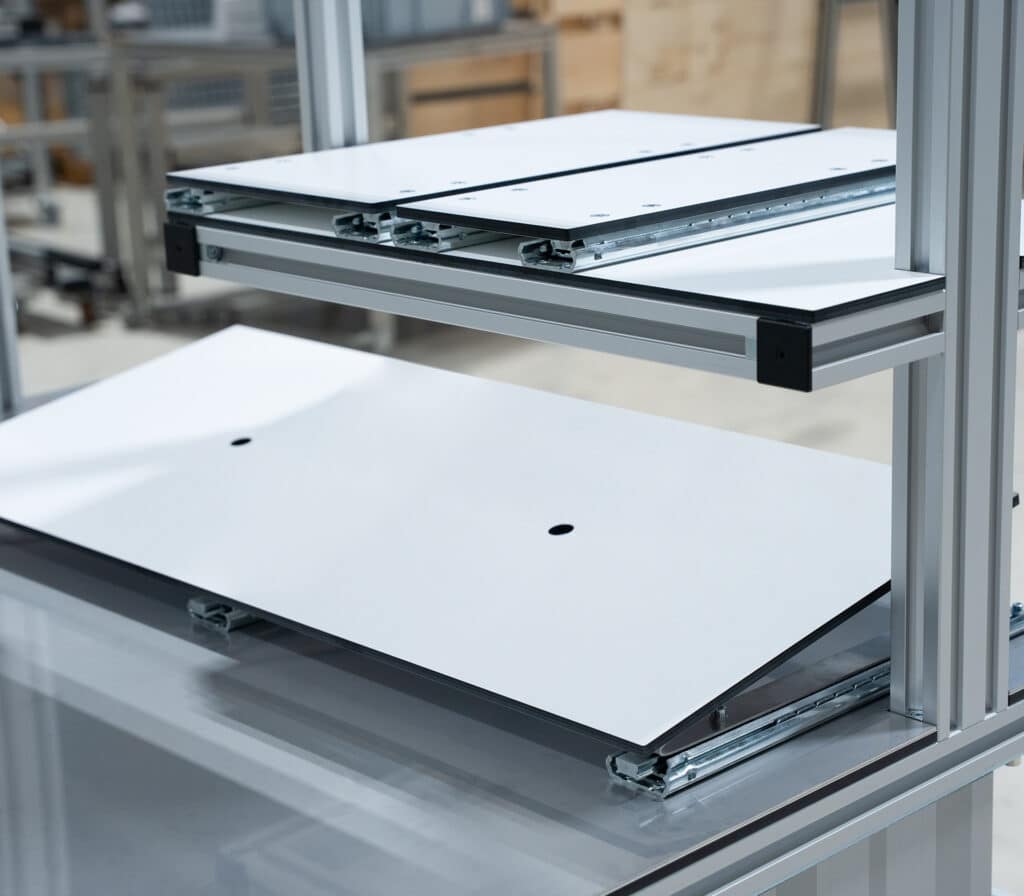 Detailansicht eines modularen Robotunits-Arbeitsplatzsystems mit ausziehbaren Ablagen auf Teleskopschienen. Die weißen Ablageflächen lassen sich flexibel herausziehen und bieten eine ergonomische Lösung für den Zugriff auf Werkzeuge oder Bauteile. Ideal zur Integration in Montagearbeitsplätze oder Materialbereitstellungssysteme.